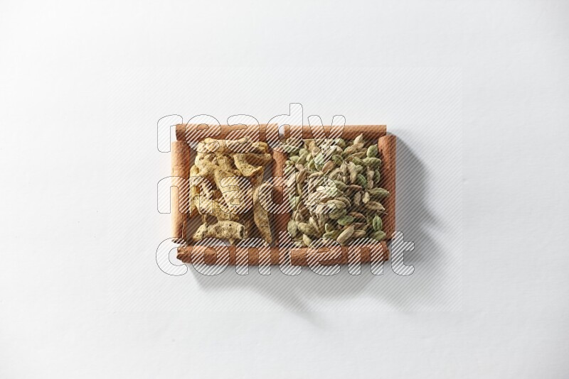 مربعان من أعواد القرفة ممتلئان بحبوب الهيل وأصابع الكركم علي خلفية بيضاء