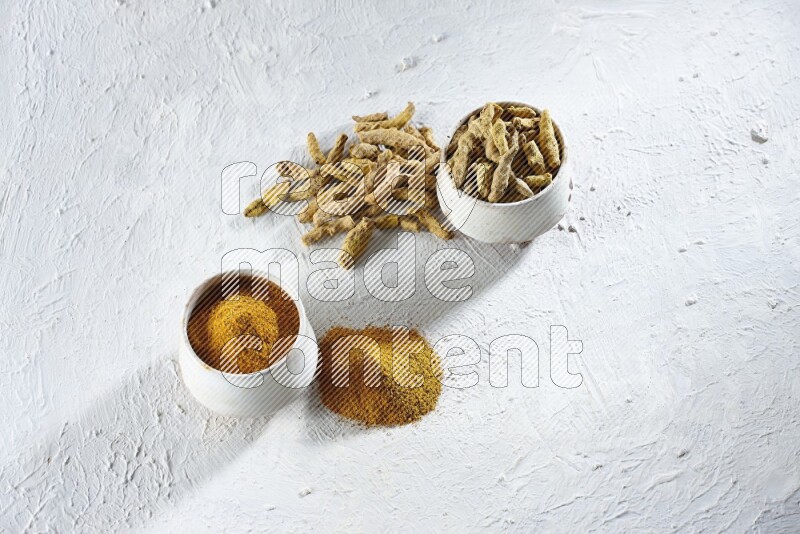 2 beige pottery bowls full of turmeric powder and dried turmeric whole fingers with powder and fingers next of it textured white flooring