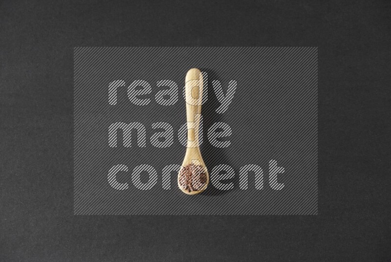 ملعقة خشبية ممتلئة بحبوب بذر الكتان علي خلفية سوداء