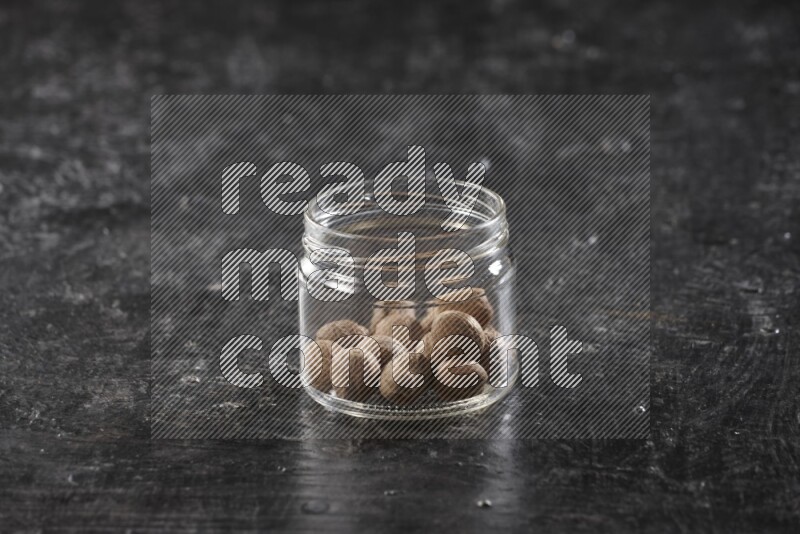 A glass jar full of whole nutmeg seeds on a black flooring