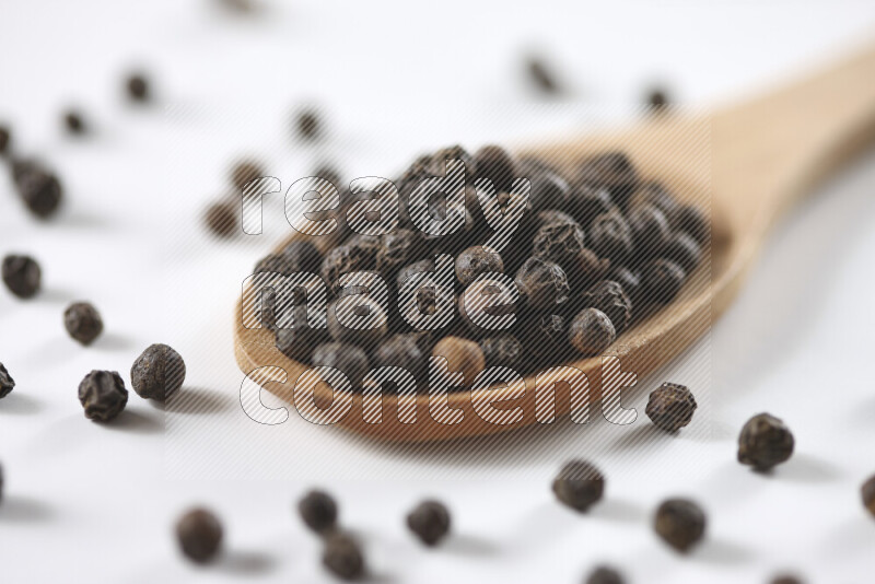 Black pepper beads with wooden spoon on white background