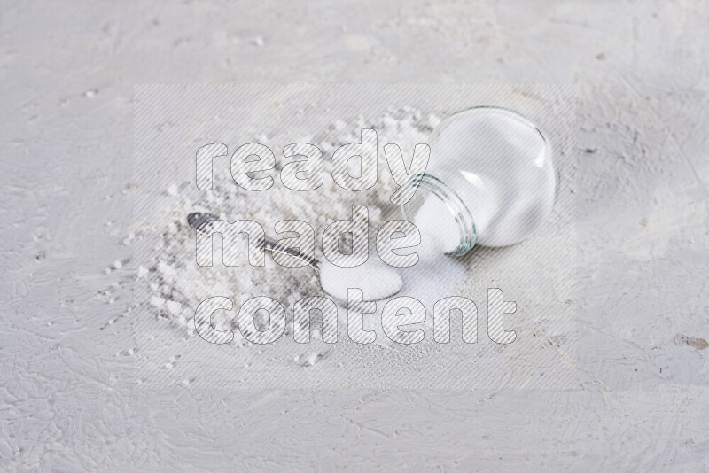 A glass jar full of table salt with some sea salt crystals beside it on a white background