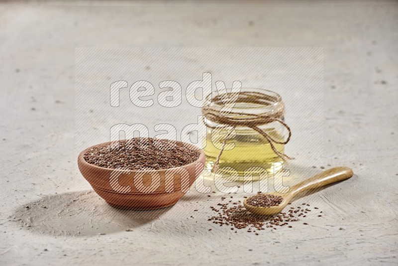 وعاء خشبي ومعلقة خشبية مليئان بحبوب بذر الكتان مع وعاء زجاجي من زيت بذر الكتان علي خلفية بيضاء