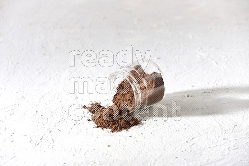 A flipped glass jar full of cloves powder on a textured white flooring