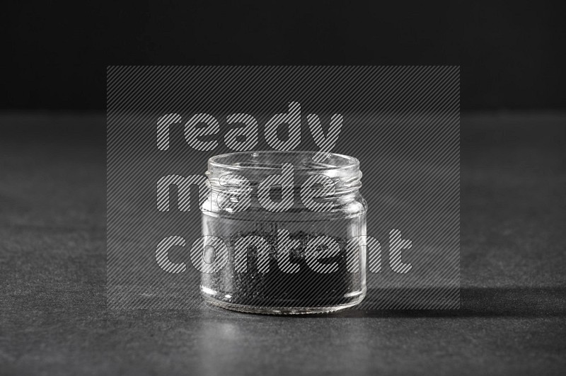 A glass jar full of black seeds on a black flooring