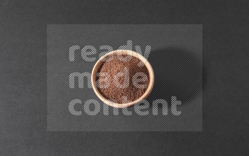 A wooden bowl full of garden cress seeds on a black flooring