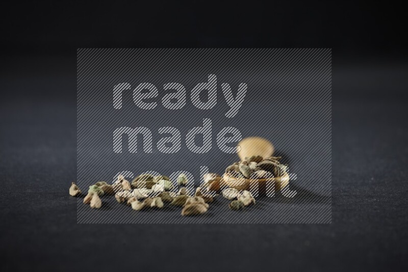 A wooden spoon full of cardamom on black flooring