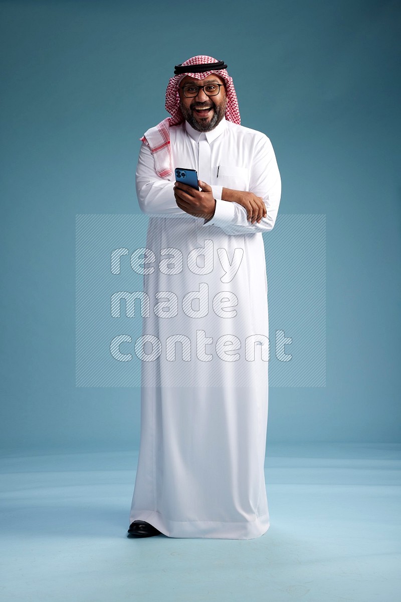 Saudi Man with shimag Standing texting on phone on blue background