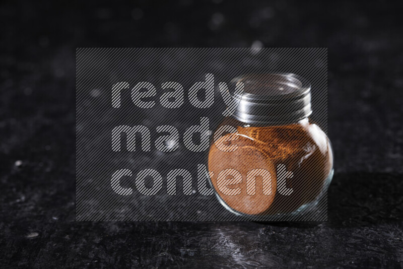 A glass jar full of ground paprika powder on black background