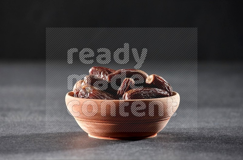 A wooden bowl full of dried dates on a black background in different angles