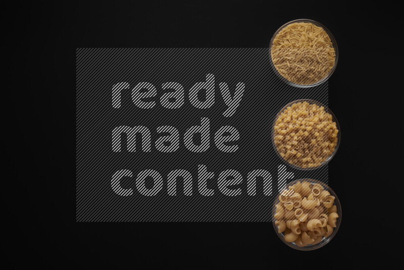 Different pasta types in 3 glass bowls on black background