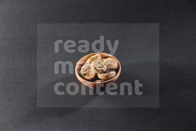 A wooden bowl full of dried figs on a black background in different angles
