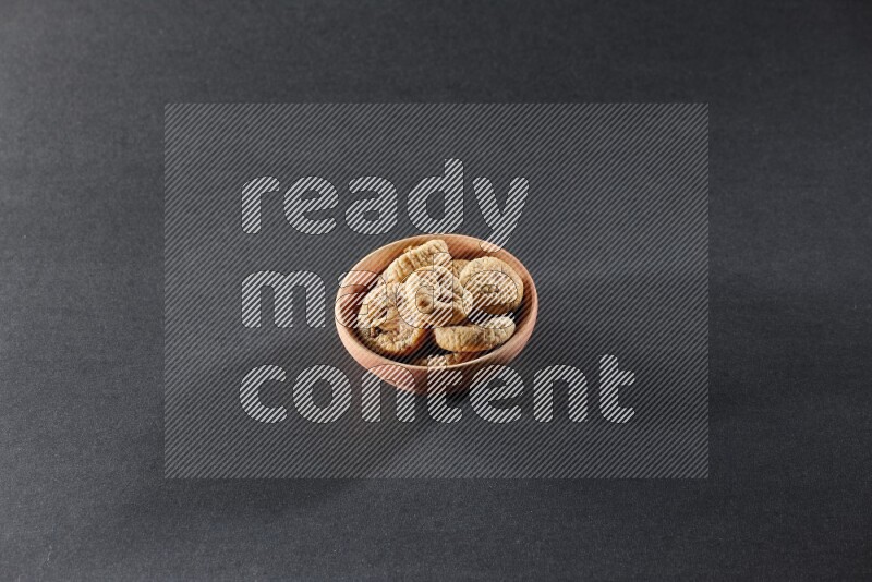 A wooden bowl full of dried figs on a black background in different angles