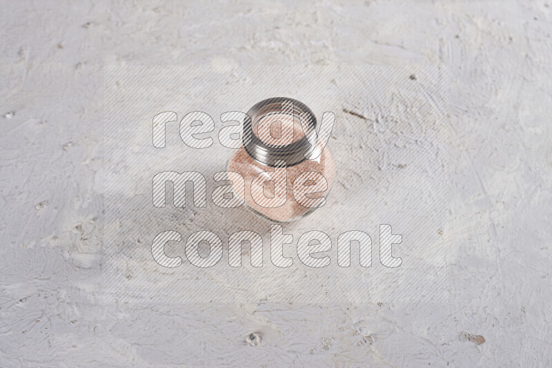 A glass jar full of fine himalayan salt on white background