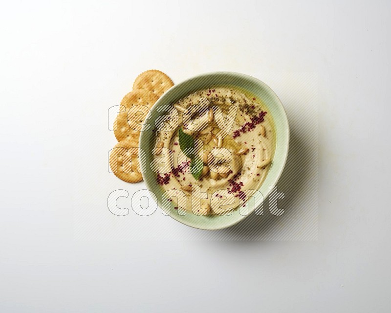 Hummus in a green plate garnished with zattar & sumak on a white background