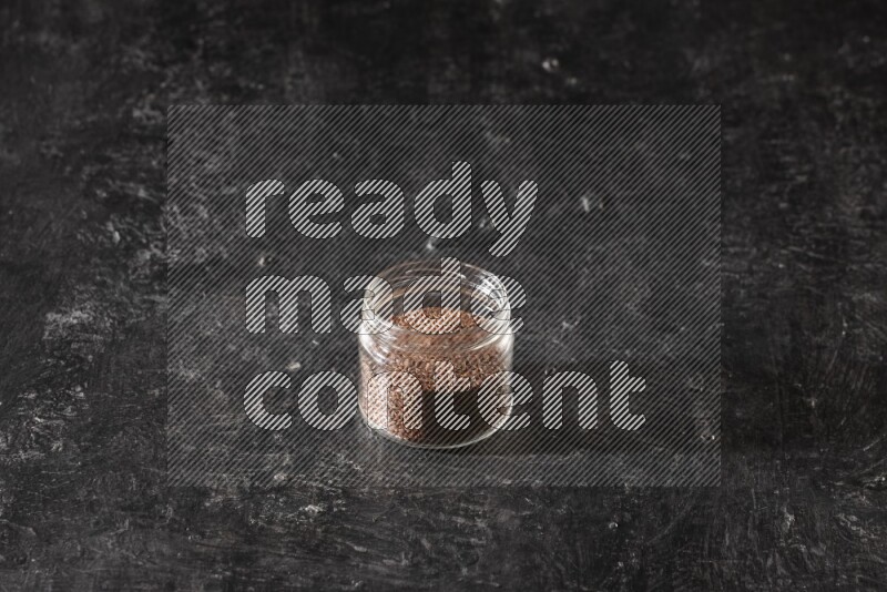 A glass jar full of flaxseeds on a textured black flooring