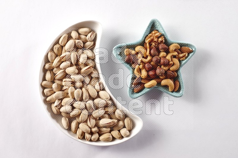 Pistachios in a crescent pottery plate and a star shaped plate with mixed nuts on white background