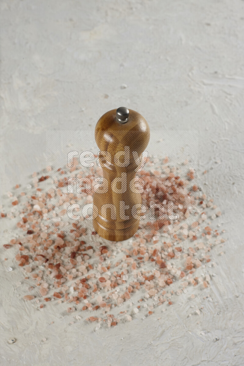 A wooden grinder standing upright and surrounded by coarse pink himalayan salt on white background