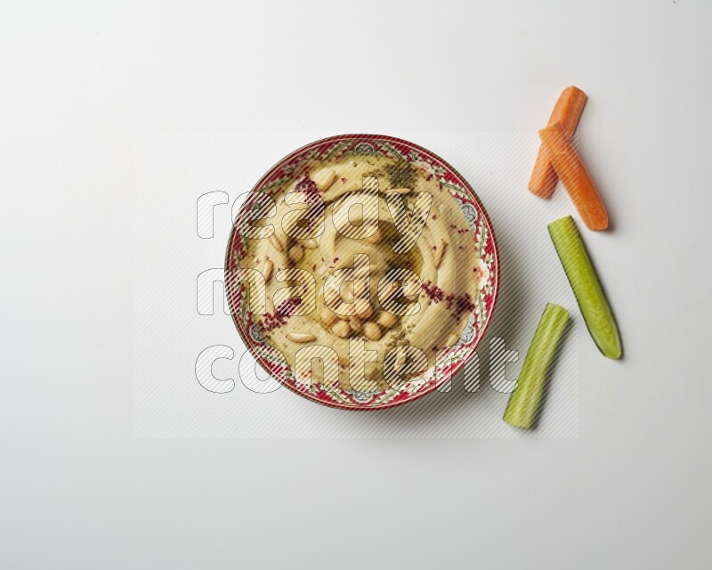Hummus in a red plate with patterns garnished with zaatar & sumak on a white background
