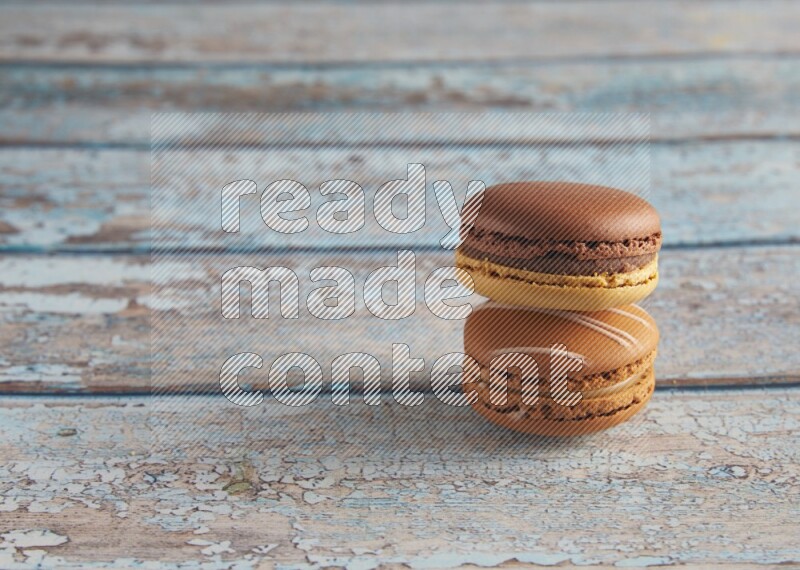 45º Shot of of two assorted Brown Irish Cream, and Yellow, and Brown Chai Latte macarons  on light blue background