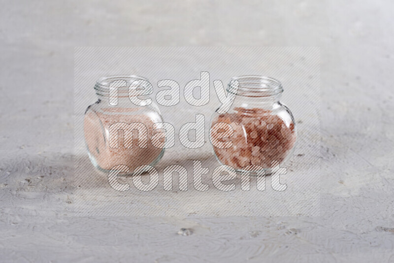 2 glass jars one is filled with fine himalayan salt and the other with coarse himalayan salt on white background