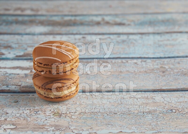 45º Shot of of two assorted Brown Irish Cream, and light brown Almond Cream macarons next to each other on light blue background