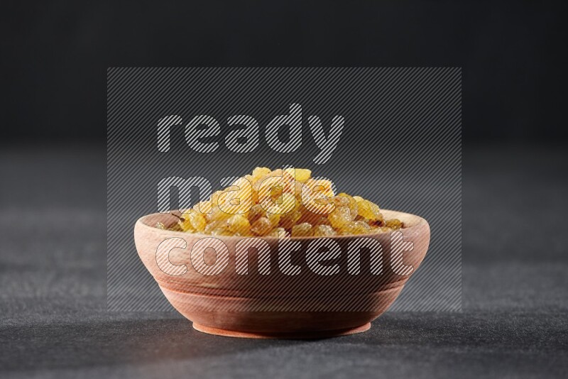 A wooden bowl full of raisins on a black background in different angles