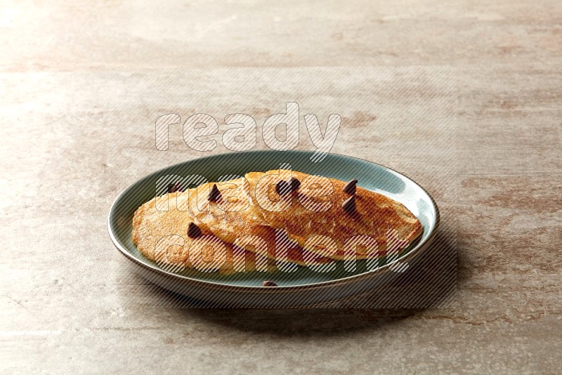Three stacked chocolate chips pancakes in a blue plate on beige background