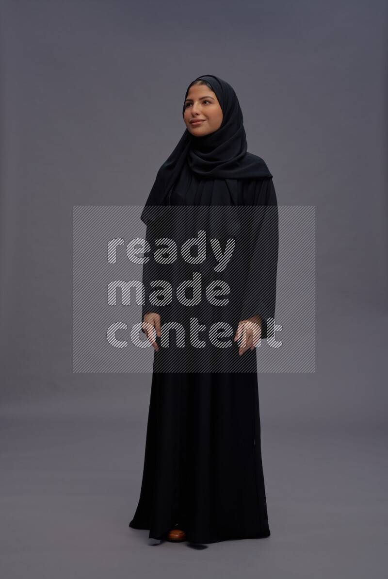 Saudi woman wearing Abaya standing interacting with the camera on gray background