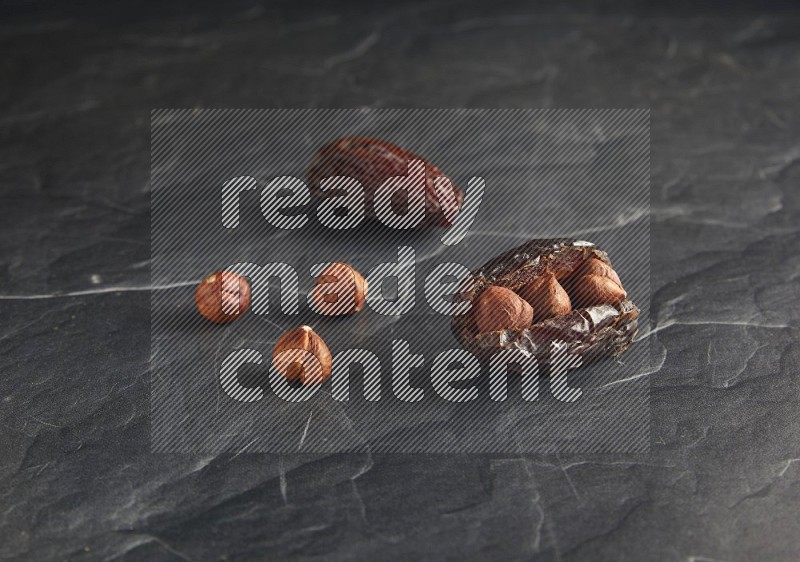 two hazelnuts stuffed madjoul dates on a black textured background