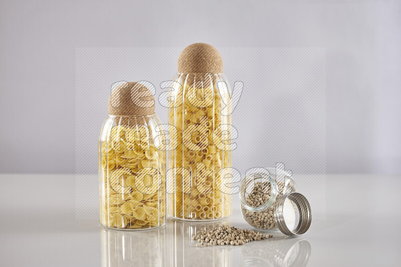 Raw pasta in glass jars with white peppers on light grey background