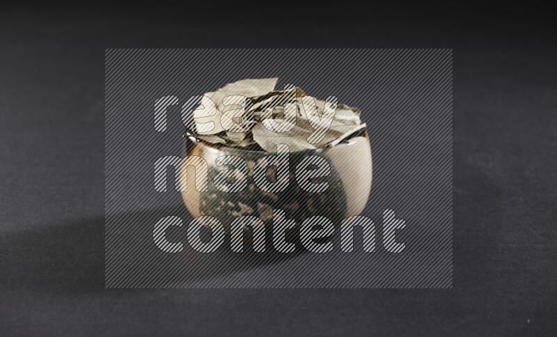 وعاء فخاري متعدد الألوان ممتلئ بأوراق الغار المجففة على أرضية سوداء