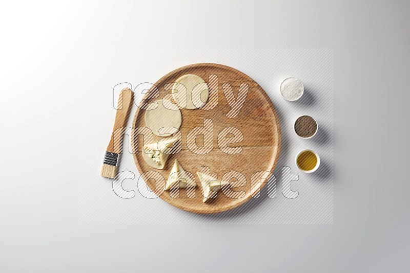 two closed sambosas and one open sambosa filled with cheese while salt, black pepper and oil with oil brush aside in a wooden dish on a white background