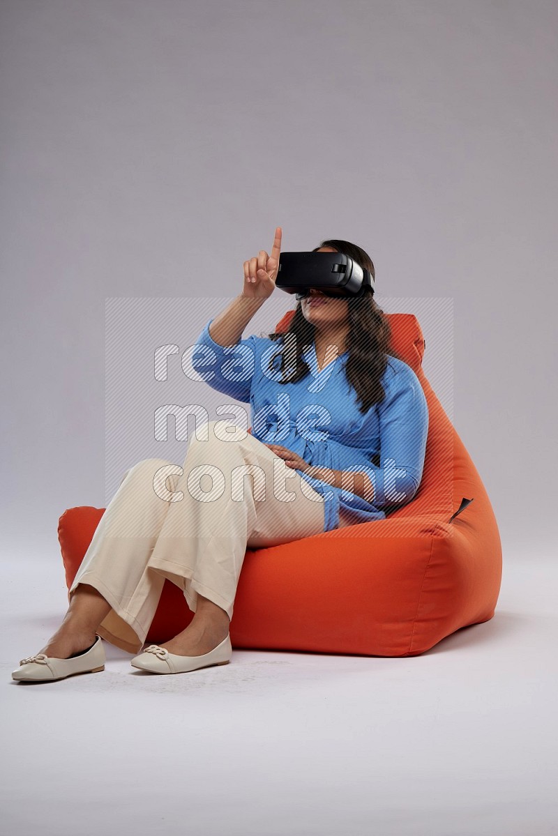 A woman sitting on an orange beanbag and gaming with VR