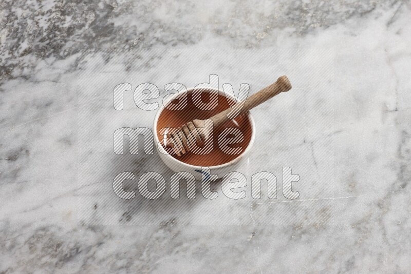 Multicolored pottery bowl with wooden honey dipper in it on grey marble background
