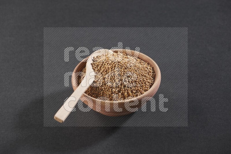 A wooden bowl and spoon full of mustard seeds on a black flooring