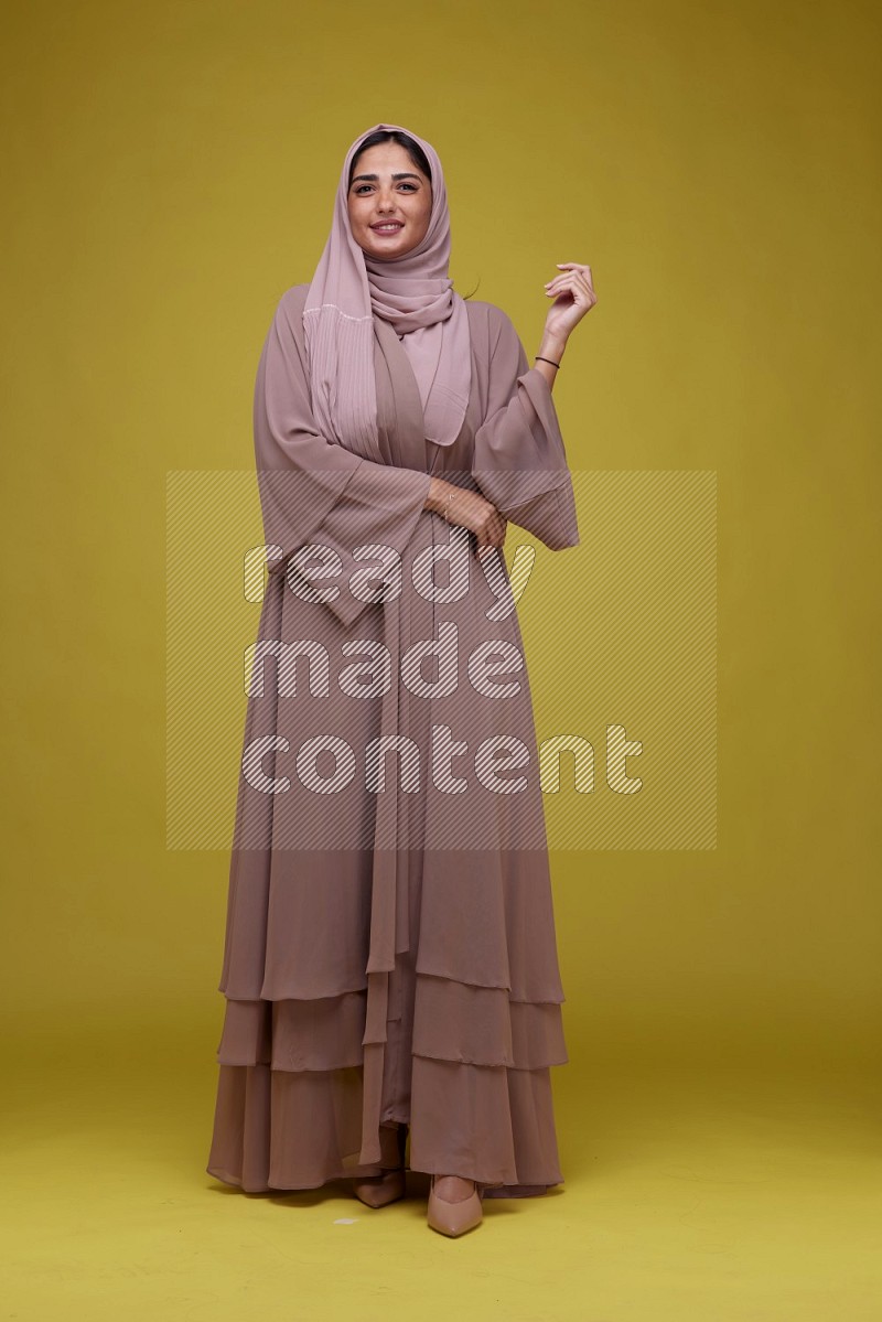 A woman Posing on a Yellow Background wearing Brown Abaya with Hijab