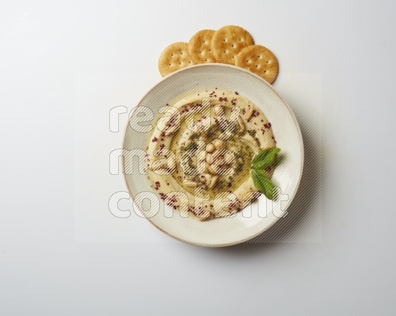 Hummus in a pottry plate garnished with zaatr & sumak on a white background