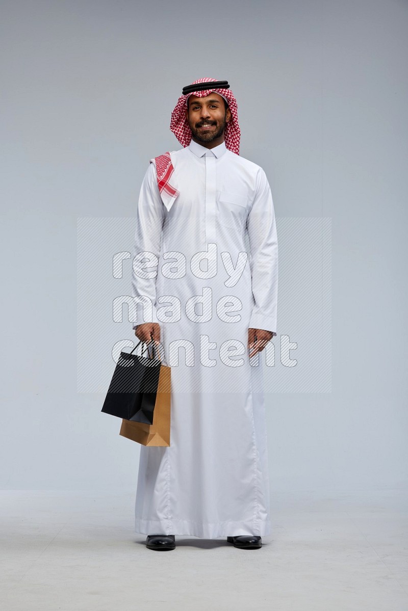 Saudi man Wearing Thob and shomag standing holding shopping bag on Gray background