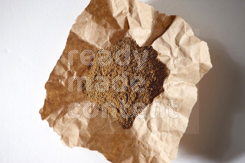 Cumin powder in a crumpled piece of paper on white flooring