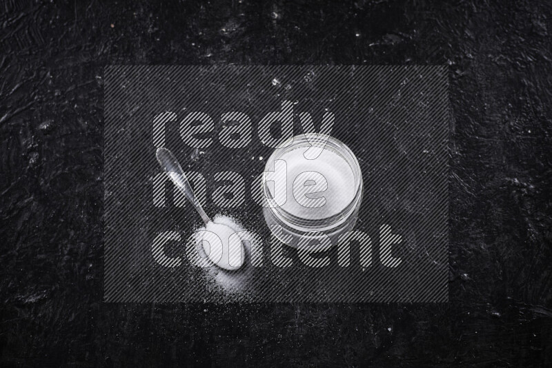 A glass jar full of fine table salt on black background