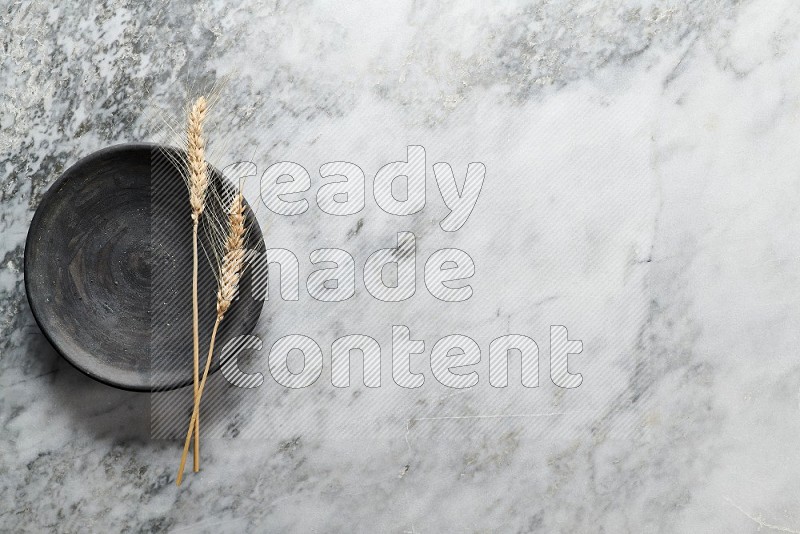 Wheat stalks on Black Pottery Plate on grey marble flooring, Top view