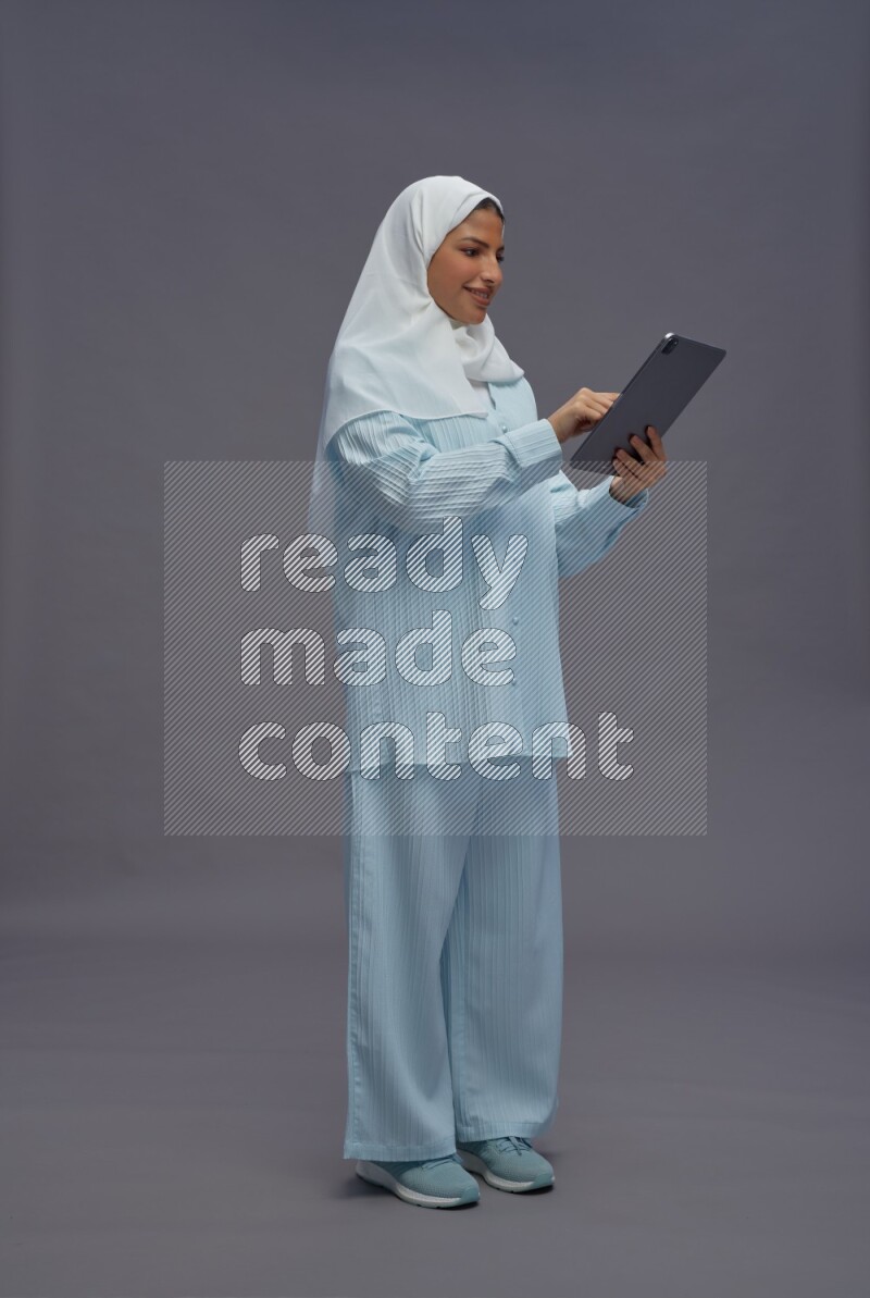 Saudi woman wearing hijab clothes standing working on tablet on gray background