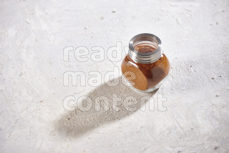 A glass jar full of ground paprika powder on white background