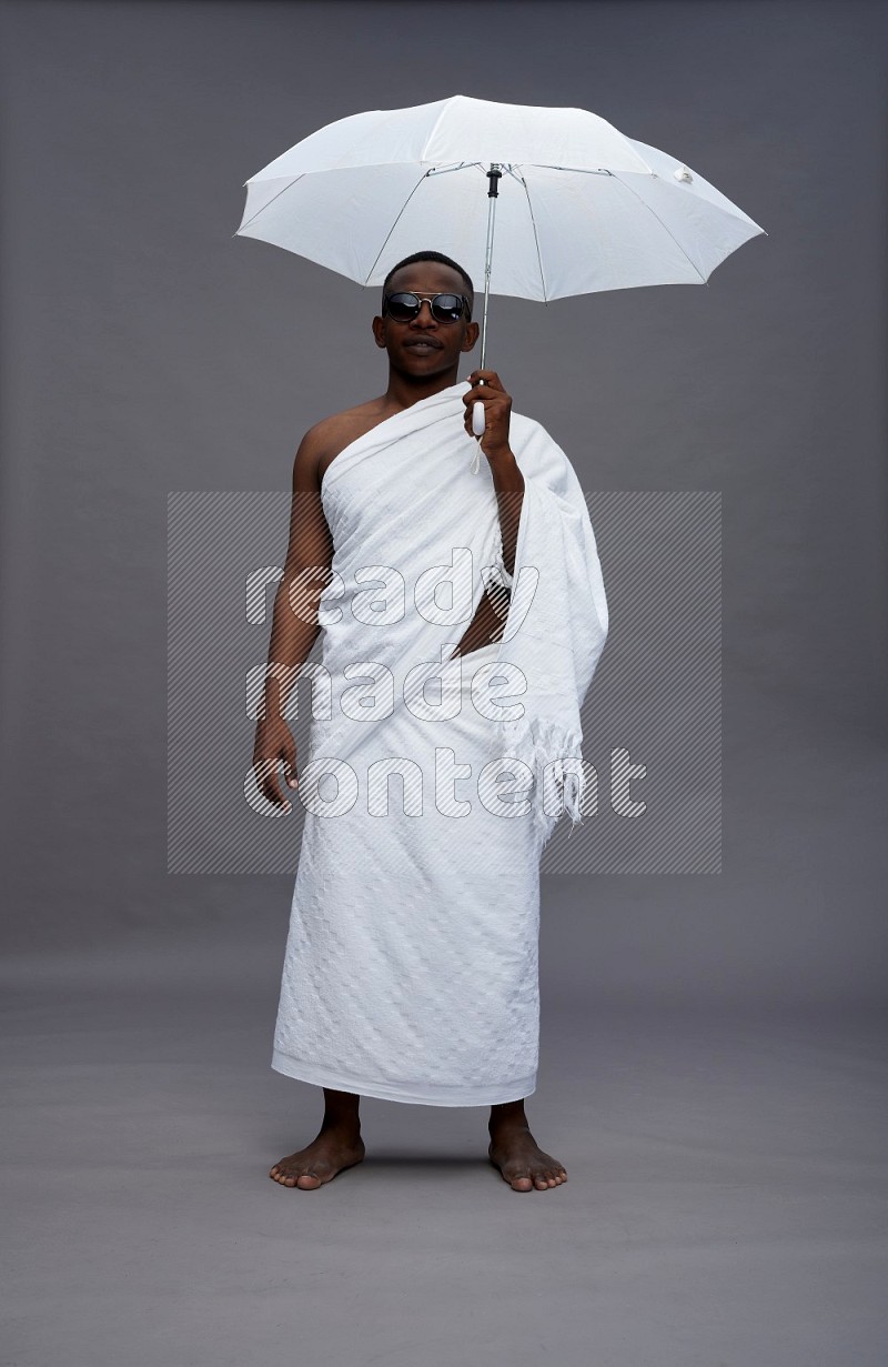 A man wearing Ehram Standing holding umbrella on gray background