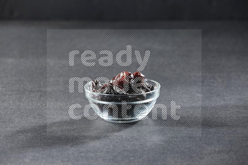 A glass bowl full of dried plums on a black background in different angles