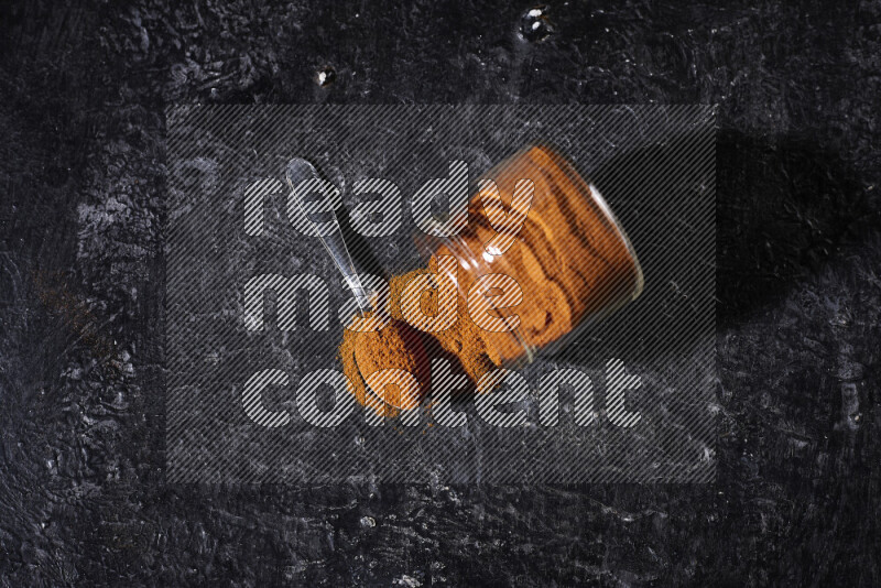 A glass jar full of ground paprika powder flipped with some spilling powder on black background