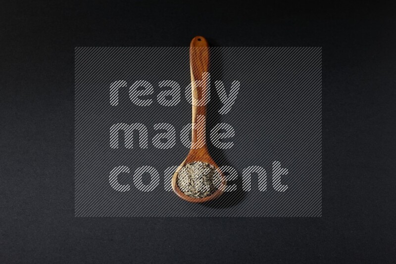 A wooden ladle full of cumin seeds on black flooring