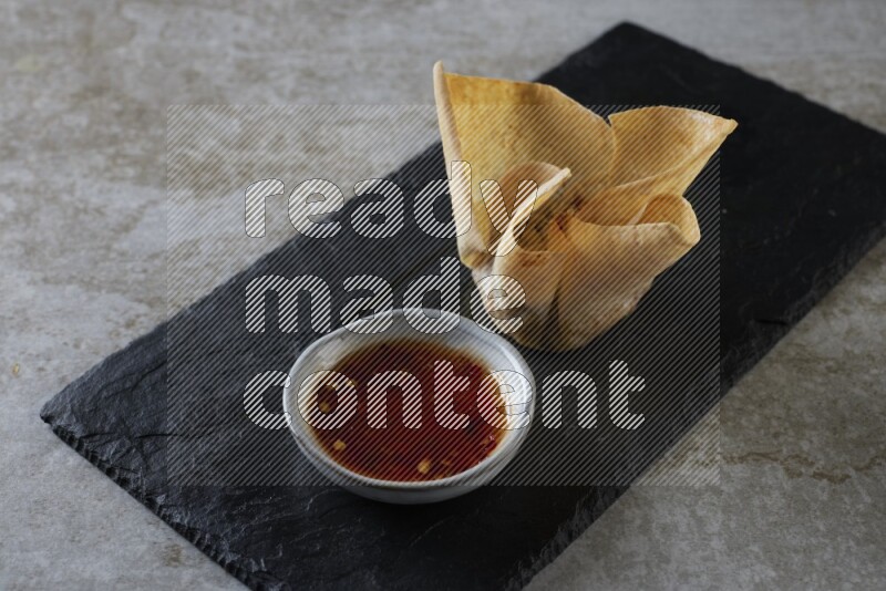 wonton cups with soy sauce ramkin on rectangle slate on grey textured counter top
