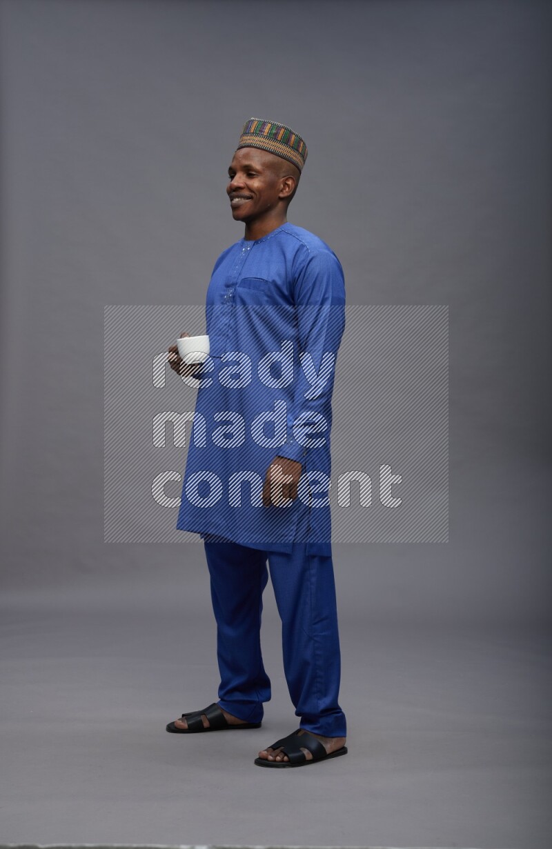 Man wearing Nigerian outfit standing holding mug on gray background